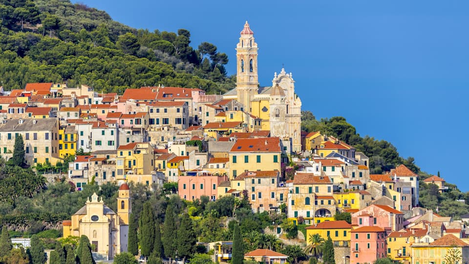 A coastal town with colorful buildings, a prominent church with a bell tower, and lush greenery on a hillside.