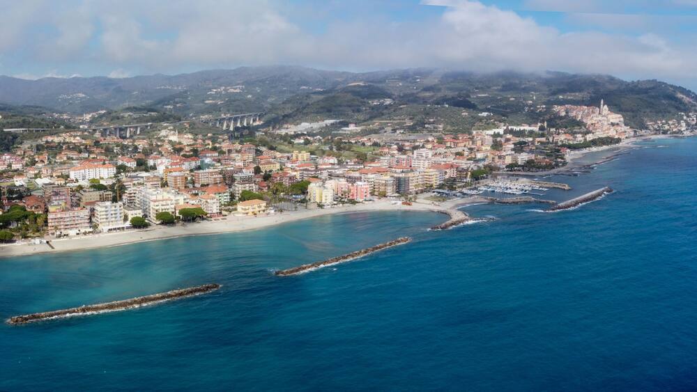 Une ville côtière avec une plage, une chaîne de montagnes et un pont en arrière-plan.
