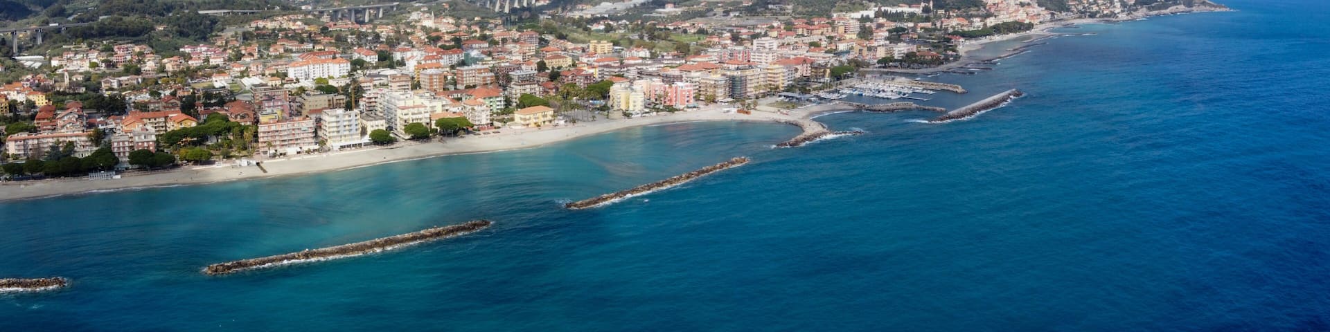 A coastal city with a beach, a mountain range, and a bridge in the background.