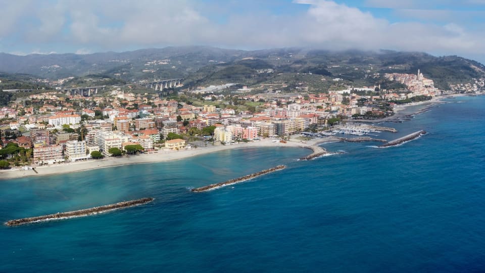 A coastal city with a beach, a mountain range, and a bridge in the background.