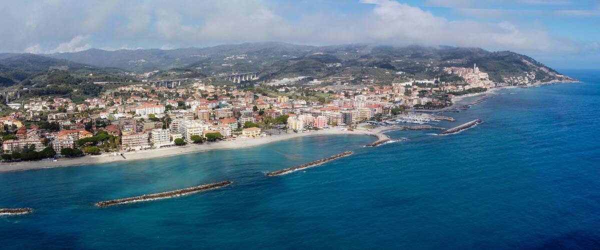 A coastal city with a beach, a mountain range, and a bridge in the background.