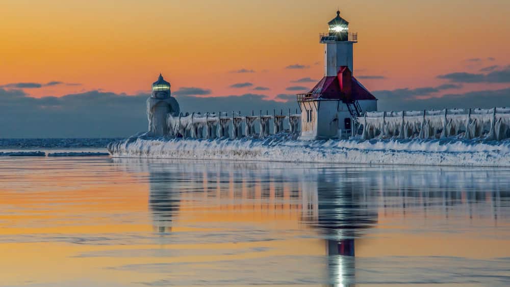 A lighthouse and ice-covered pier at sunset.