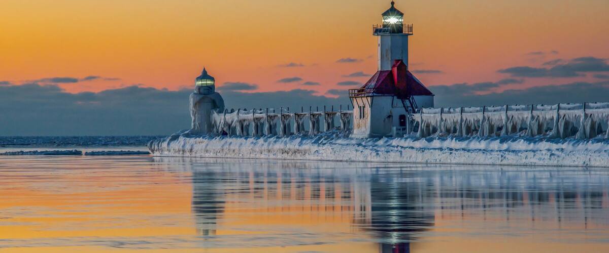 A lighthouse and ice-covered pier at sunset.