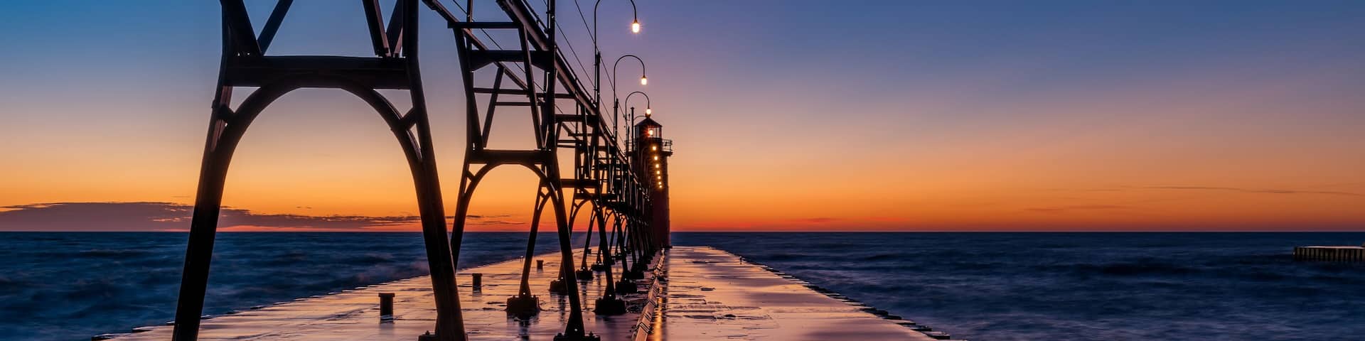 A coastal bridge at sunset with a calm sea and street lamps.
