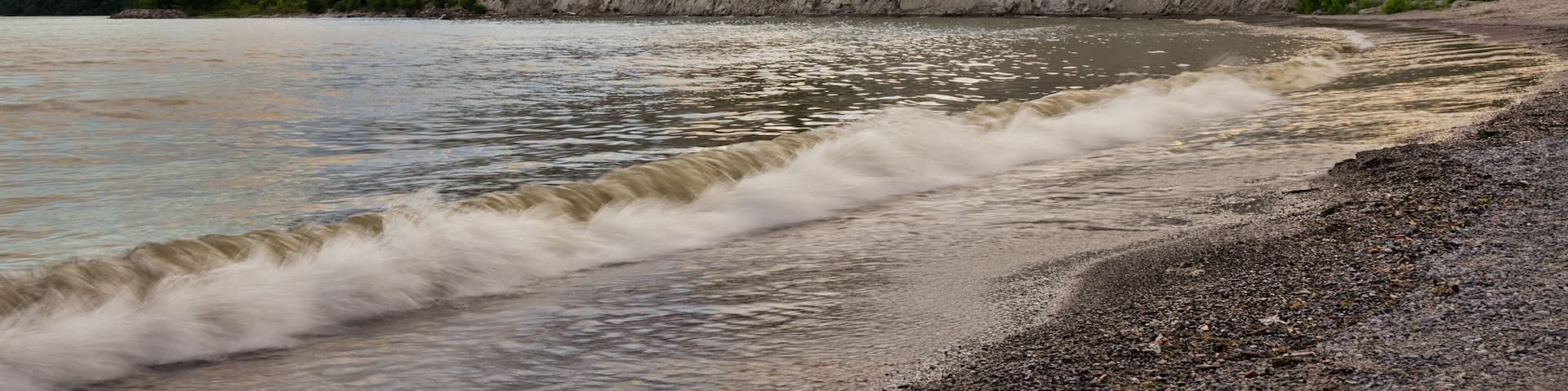 A riverbank with a rocky cliff and trees.