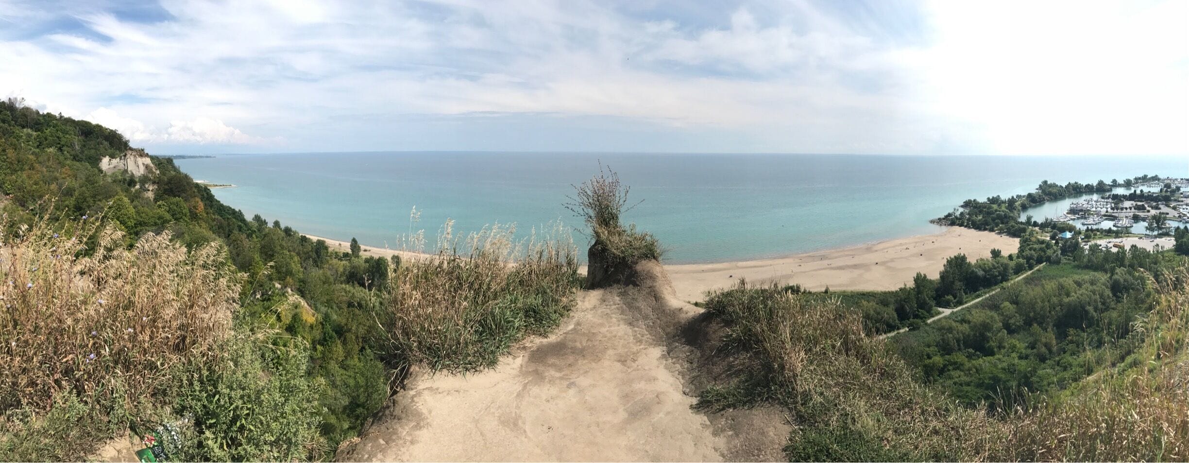 A coastal path leading to a beach with a marina and a cliff.