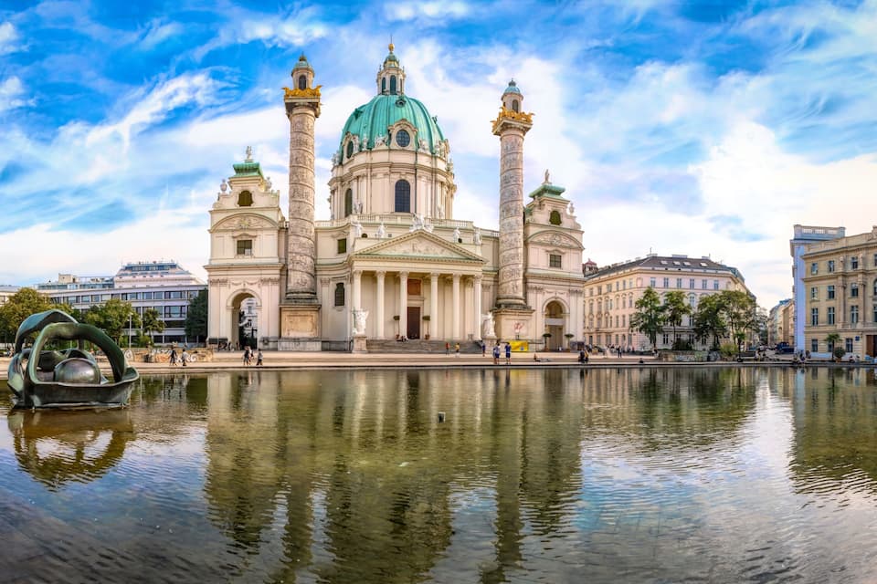 A grand cathedral with a green dome, two tall columns, and a reflection in the water.