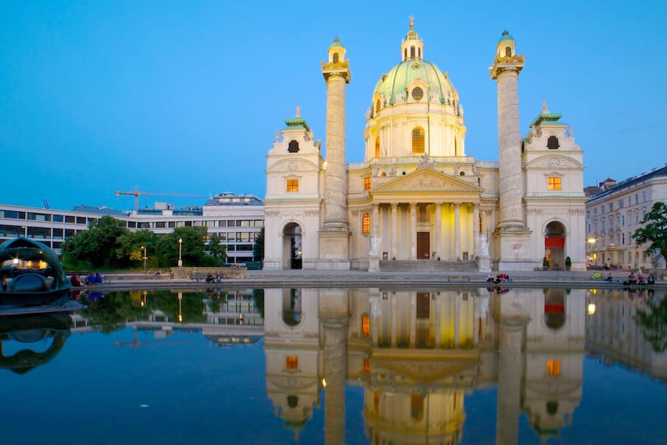 A grand cathedral with a large dome and twin towers, reflecting in a calm water body in front.