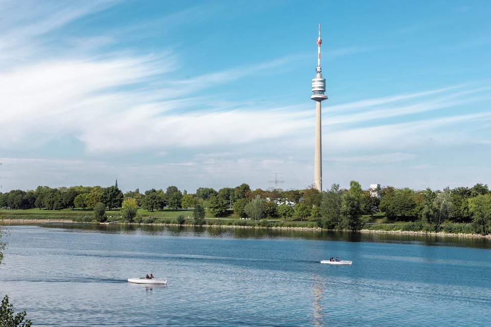 A lake with two boats, a tower, and a park with trees.