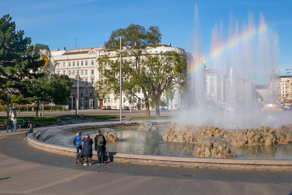 A fountain with water jets and a rainbow in an urban park.