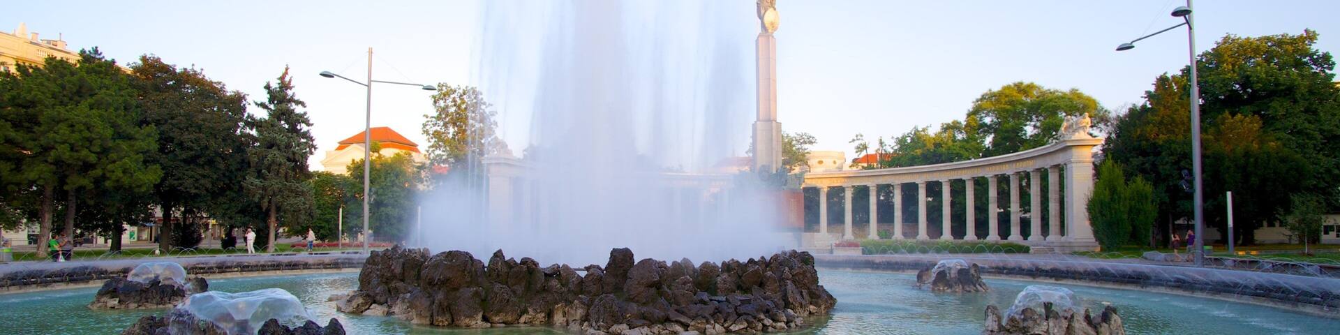 A fountain with water jets, a statue, and a neoclassical building in the background.