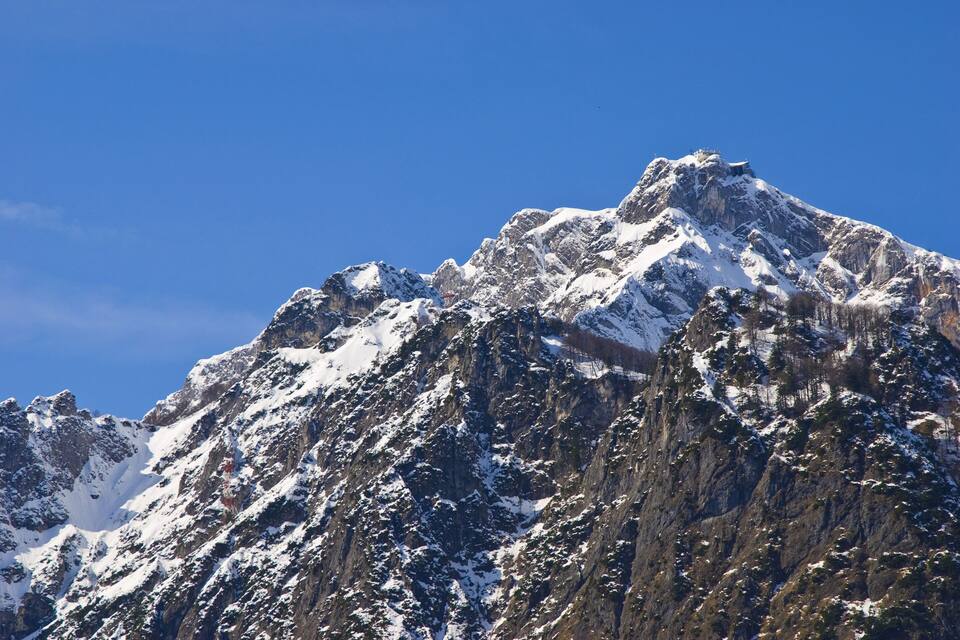 Cima montuosa innevata con terreno impervio e cielo azzurro limpido.