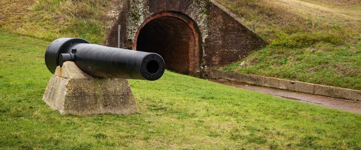 A cannon on a grassy hill with a brick structure in the background.