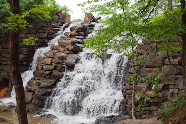 Uma cascata desce sobre um afloramento rochoso, rodeada por vegetação exuberante.