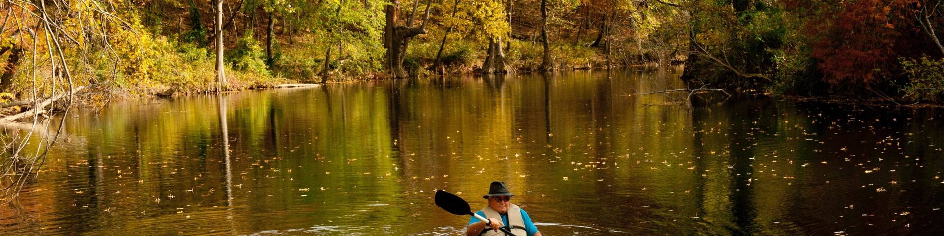 Un kayakista en un río rodeado de follaje otoñal.