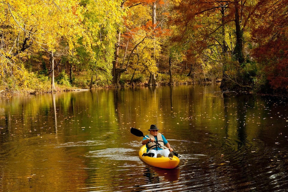 Un kayakista en un río rodeado de follaje otoñal.