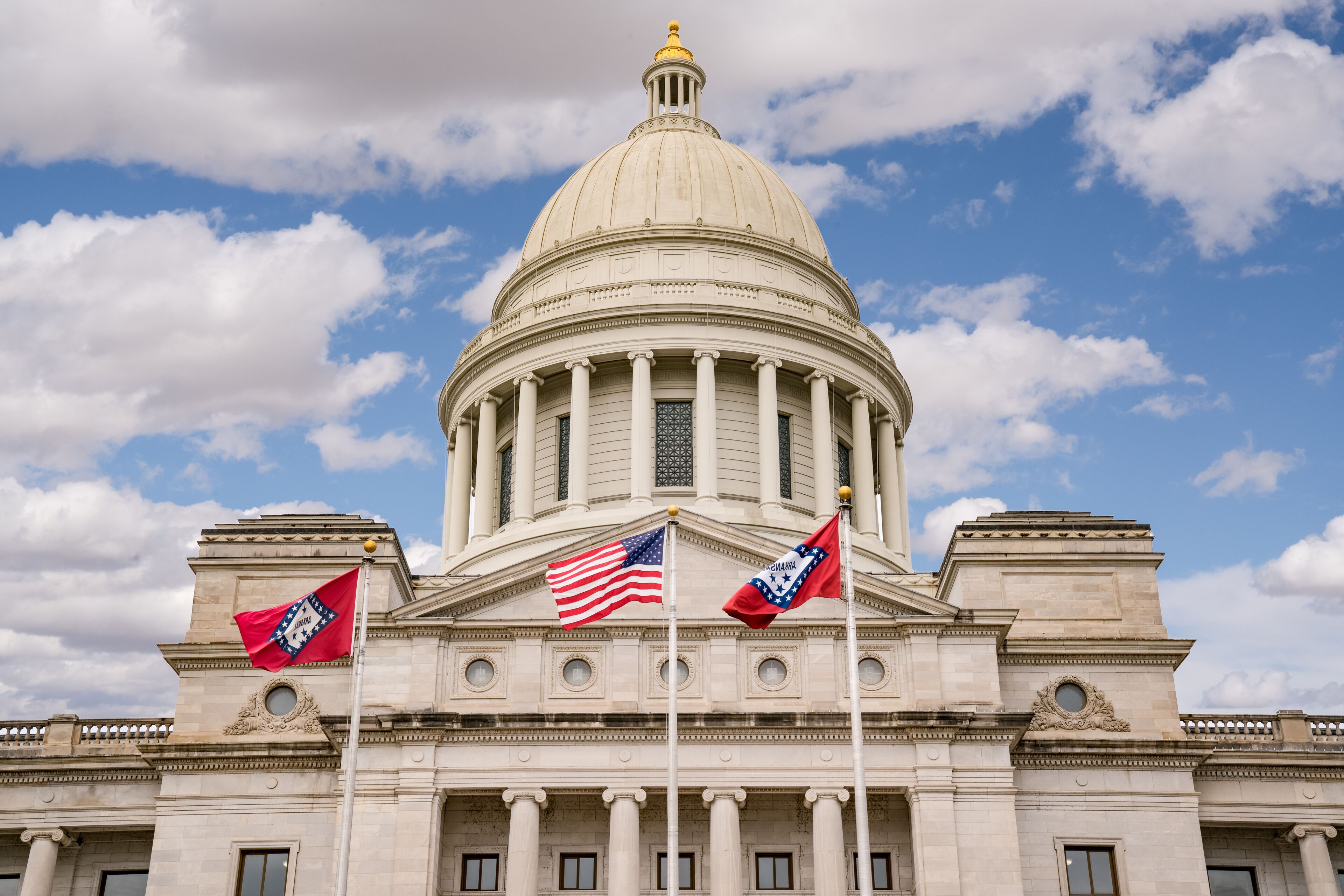 A neoclassical building with a large dome, columns, and two flags.