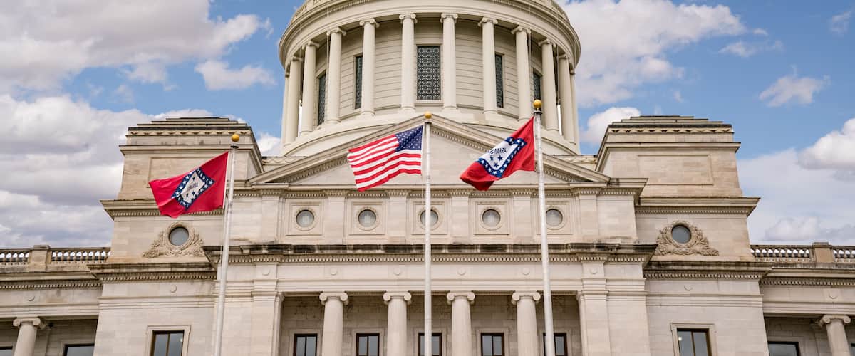 A neoclassical building with a large dome, columns, and two flags.