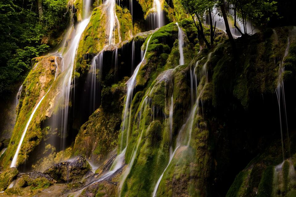 A multi-tiered waterfall surrounded by lush green foliage.