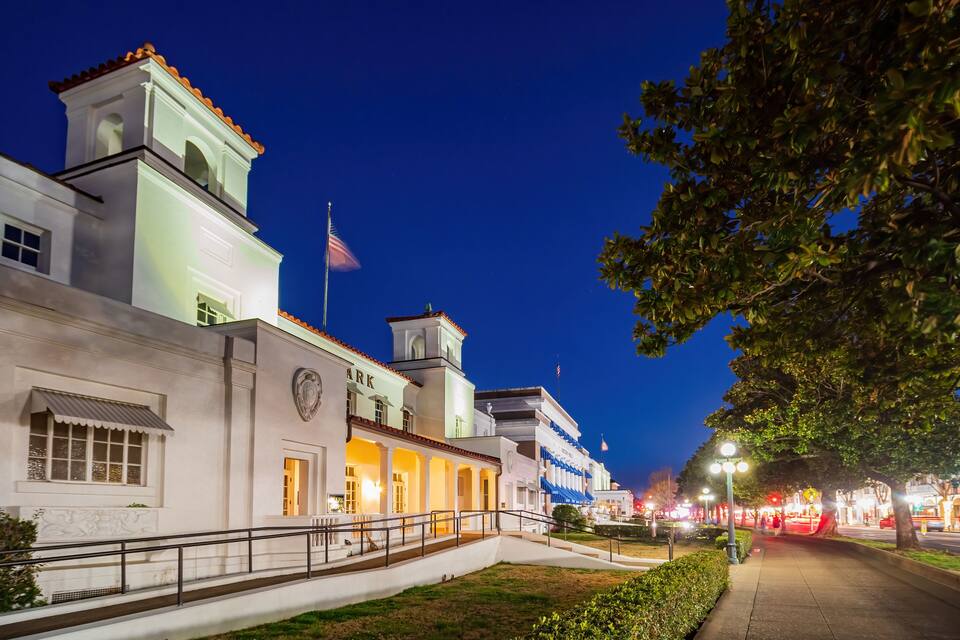 A historic building with a clock tower, a flag, and a well-lit pathway.