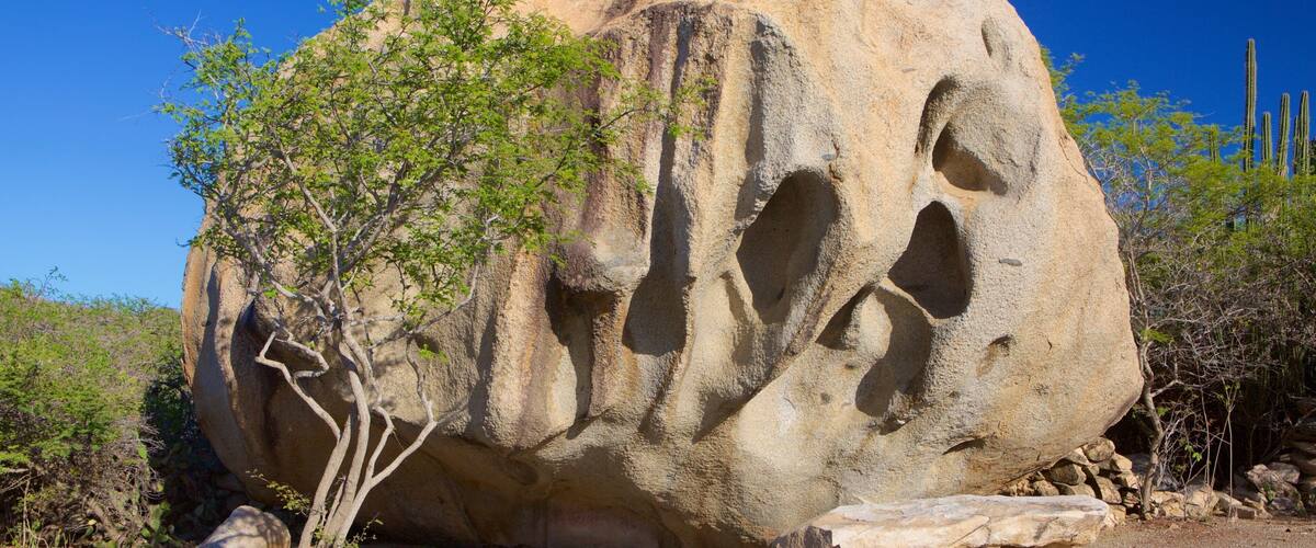 A large rock formation with multiple cavities and a bench in front.