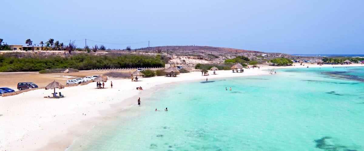 A beach with clear turquoise water, a sandy shore, and a few thatched-roof huts.