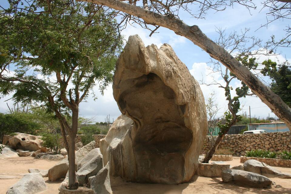 Una gran formación rocosa con un rostro tallado, rodeada de árboles y piedras.