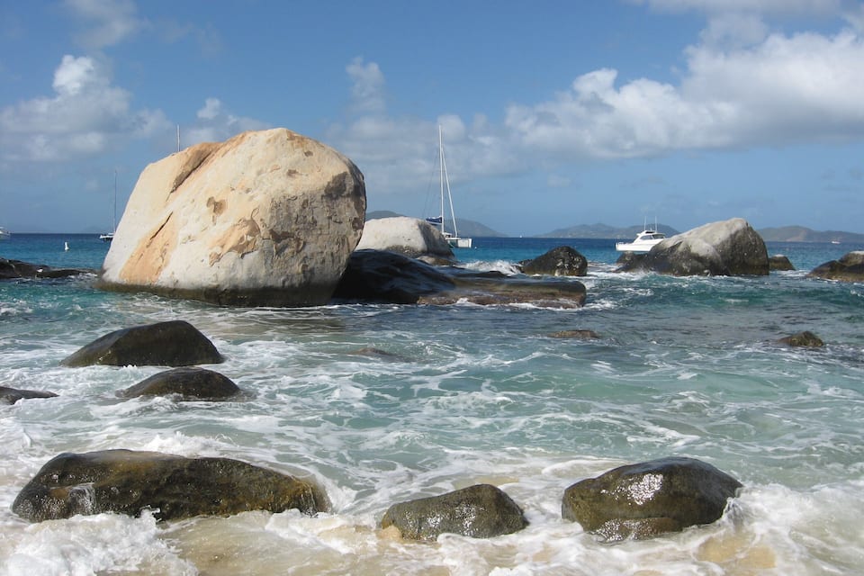 Eine felsige Küste mit großen Felsen und Booten im Hintergrund.