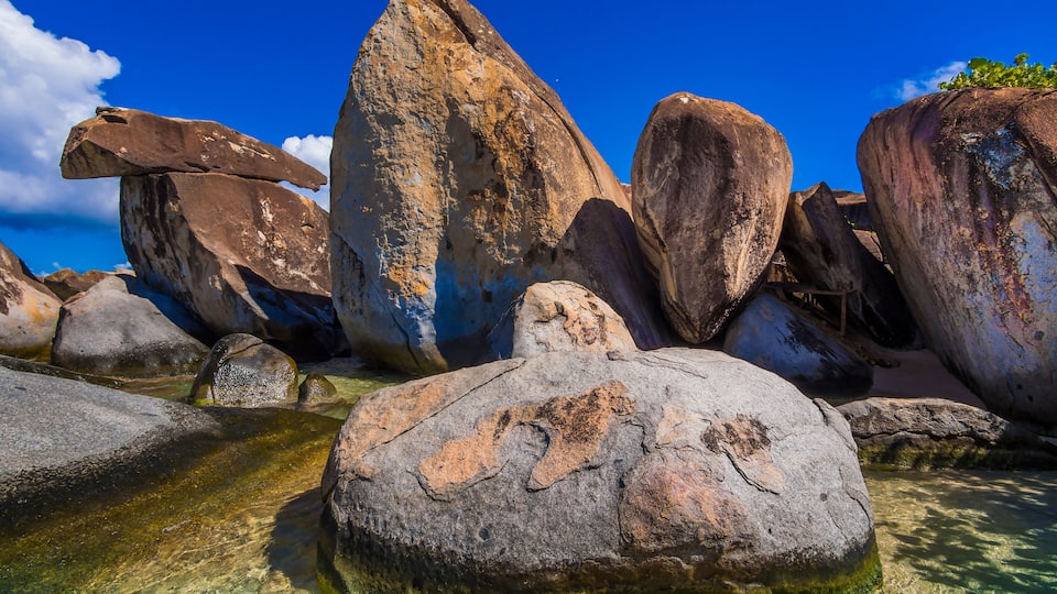 Large boulders in clear shallow water with a blue sky.