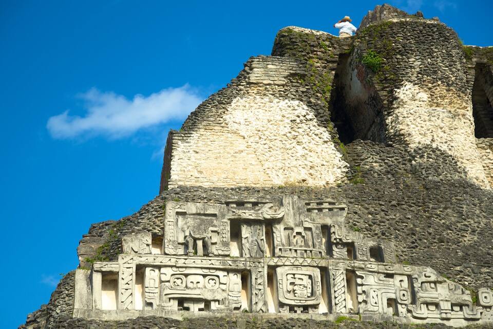 Estructura de piedra con relieves, una persona en la parte superior y cielo azul despejado.