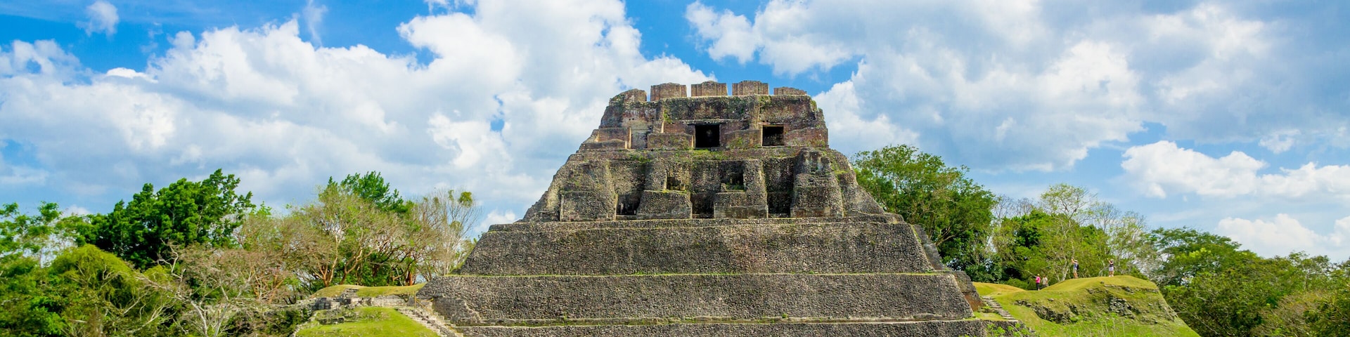 Una gran pirámide antigua con escalinatas que conducen a su cima, rodeada de exuberante vegetación y árboles.