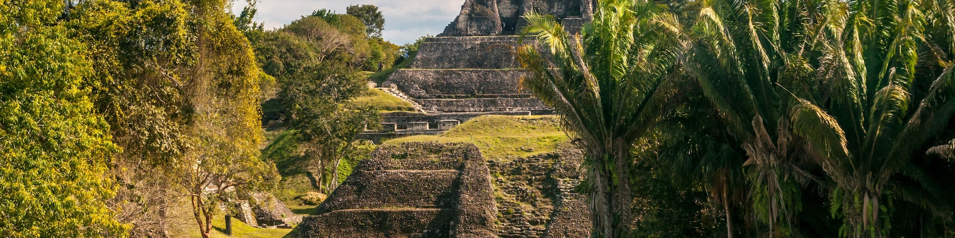 Ruinas antiguas con pirámides escalonadas y una gran estructura de piedra sobre una colina cubierta de hierba.