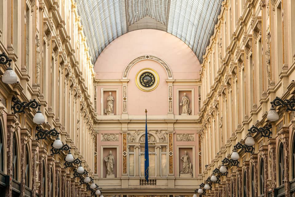 A grand architectural corridor with ornate columns, a dome ceiling, and statues.