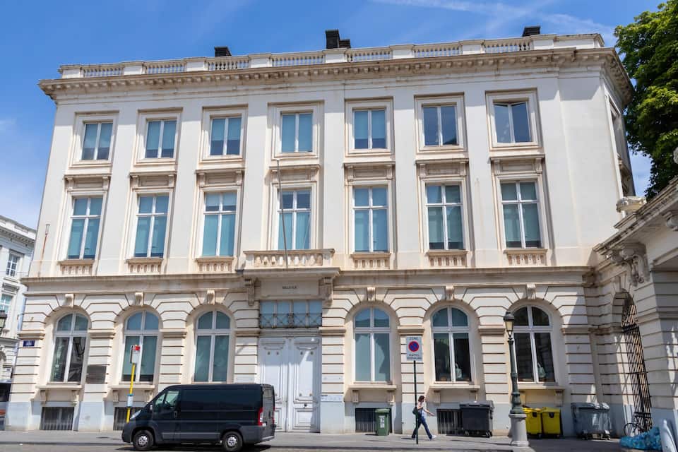 Edificio histórico con amplias ventanas y un letrero que indica zona sin estacionamiento.