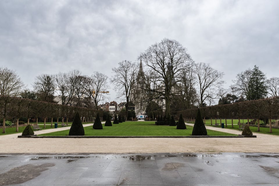 A formal garden with a symmetrical layout, featuring neatly trimmed hedges, a central lawn, and a prominent building in the background.