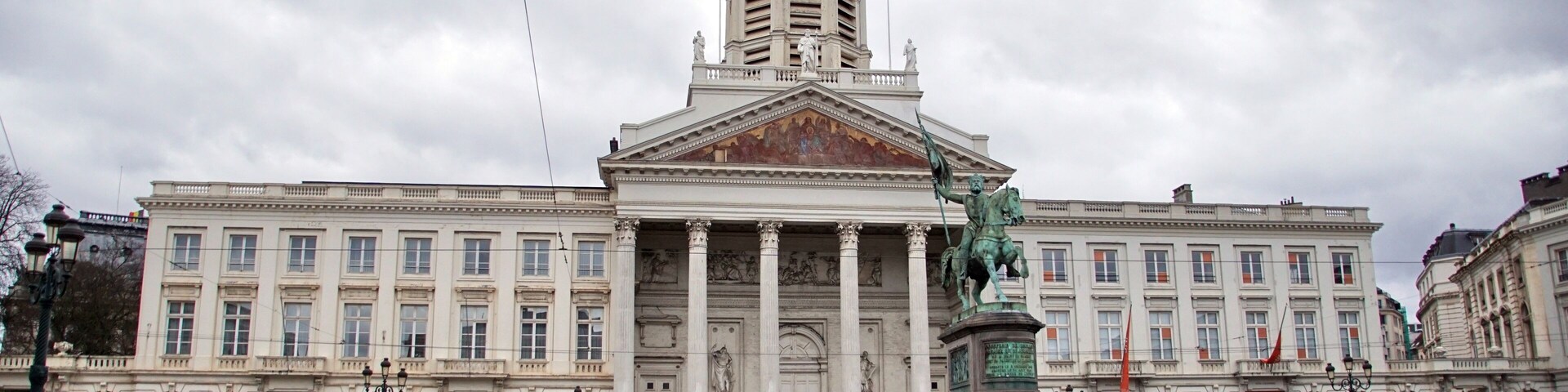 Un edificio histórico con una imponente torre del reloj y estatuas en primer plano.