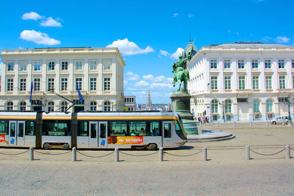 Um elétrico em uma praça da cidade, com edifícios históricos e uma estátua.