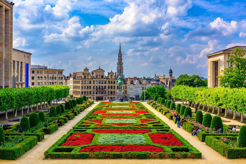 A formal garden with geometrically arranged flower beds, a prominent church spire, and classical architecture in the background.