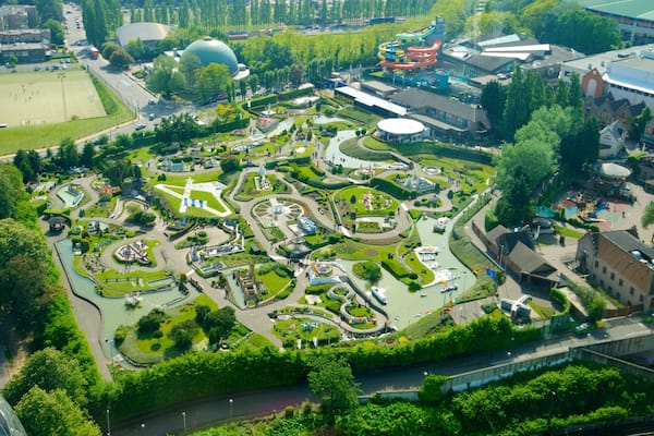 An aerial view of a park with a large lake, walking paths, and various buildings.