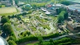 Luchtbeeld van een park met een groot meer, wandelpaden en verschillende gebouwen.