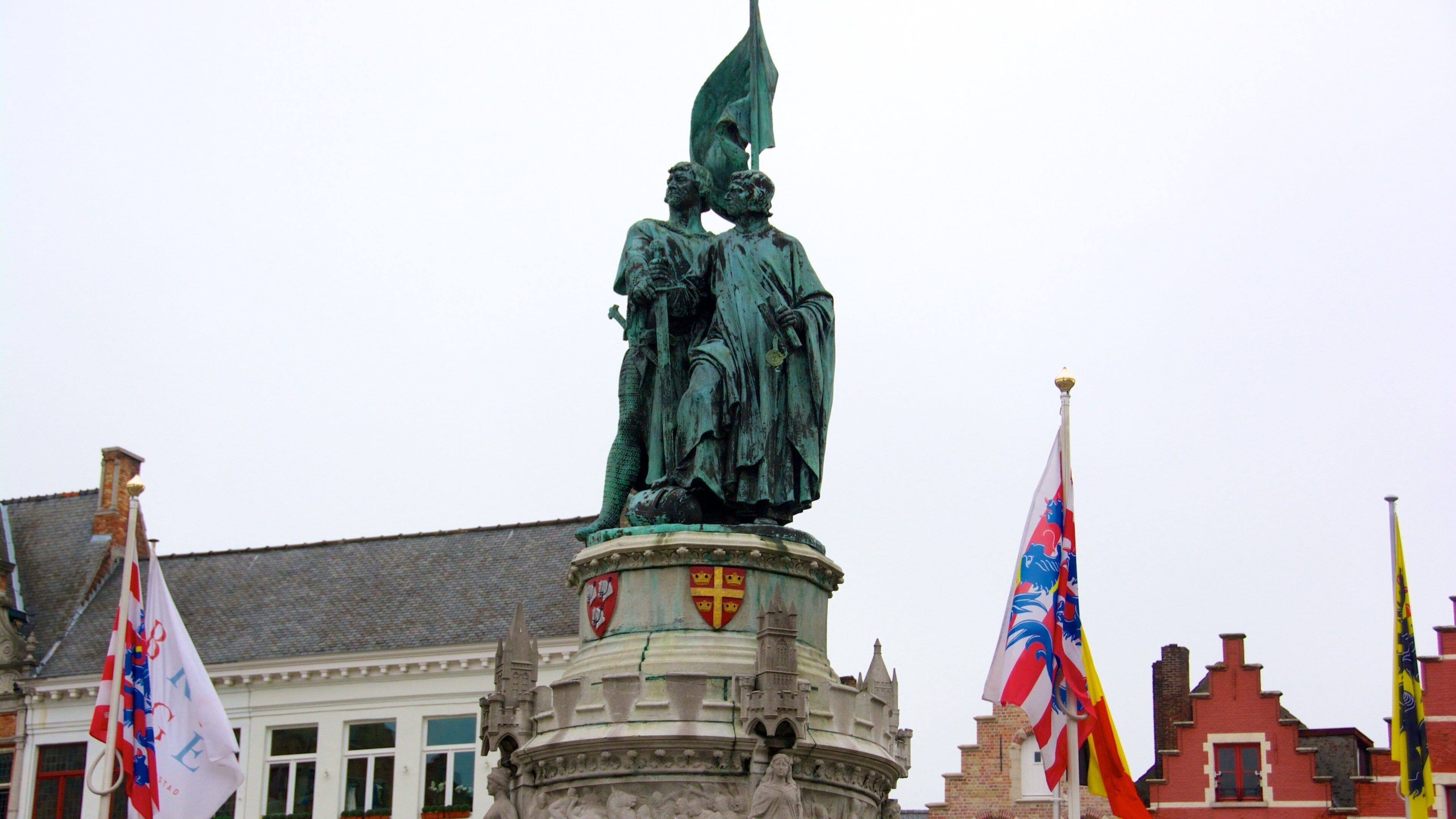 A statue of a man with a sword, surrounded by flags and a building with a tiled roof.