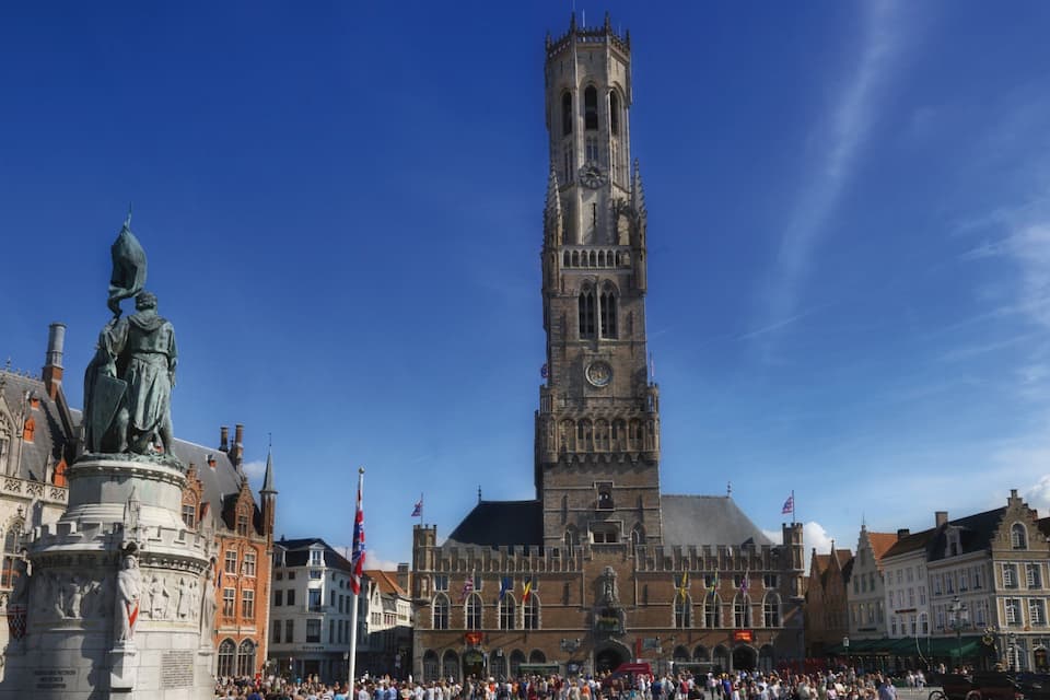Een historisch plein met een opvallende klokkentoren, een standbeeld en omliggende gebouwen.
