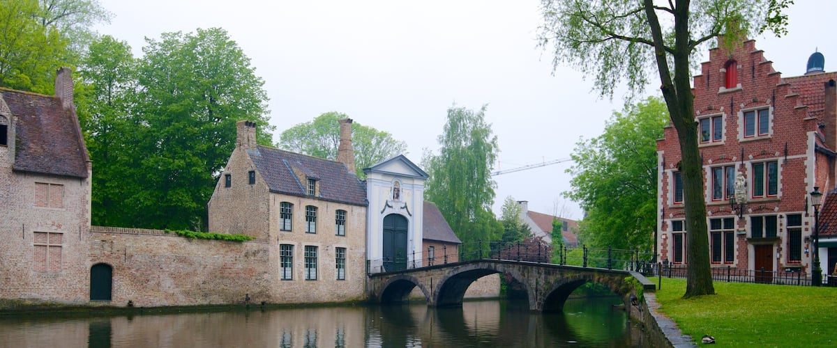 A canal with a stone bridge, brick buildings, and lush greenery.