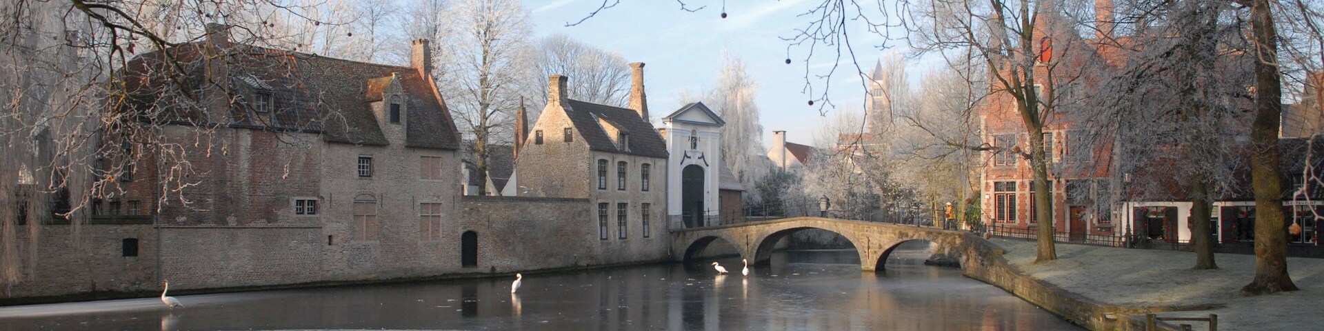 A canal with a stone bridge, historic buildings, and a statue.