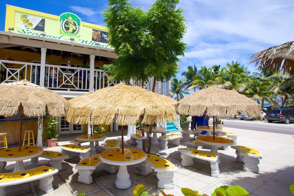 Ein Restaurant direkt am Strand, mit reetgedeckten Sonnenschirmen und gelb gefliesten Tischen.