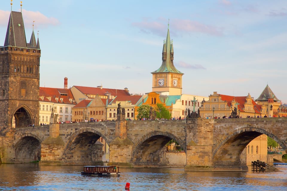 A historic stone bridge with multiple arches over a river, a prominent clock tower, and traditional buildings with red roofs.