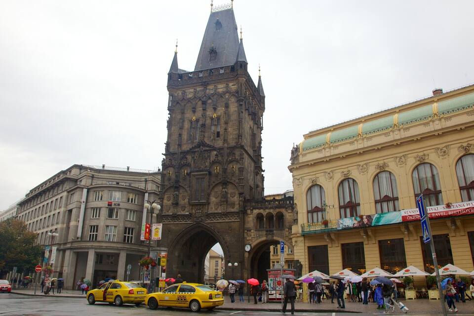 A historic building with a tall tower, a modern yellow taxi, and a building with green awnings.