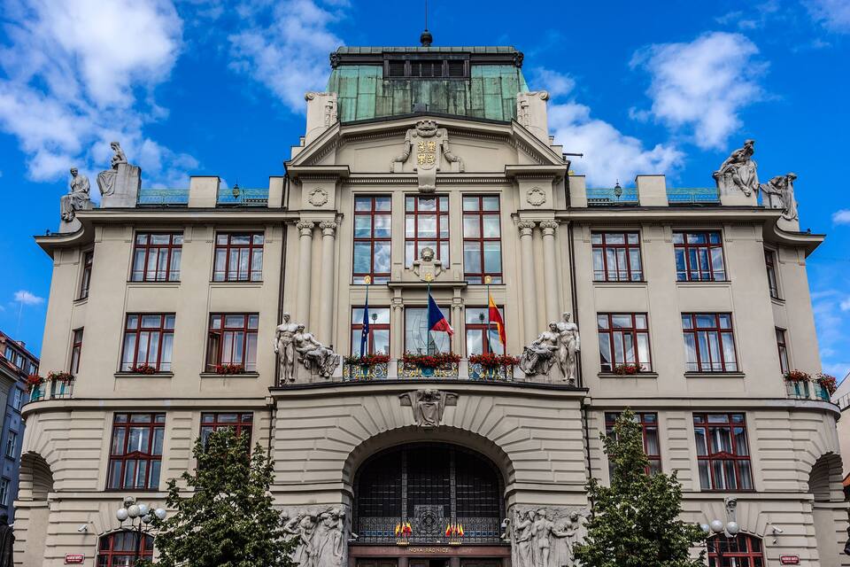 Un edificio histórico con esculturas ornamentales, un gran arco de entrada y banderas.