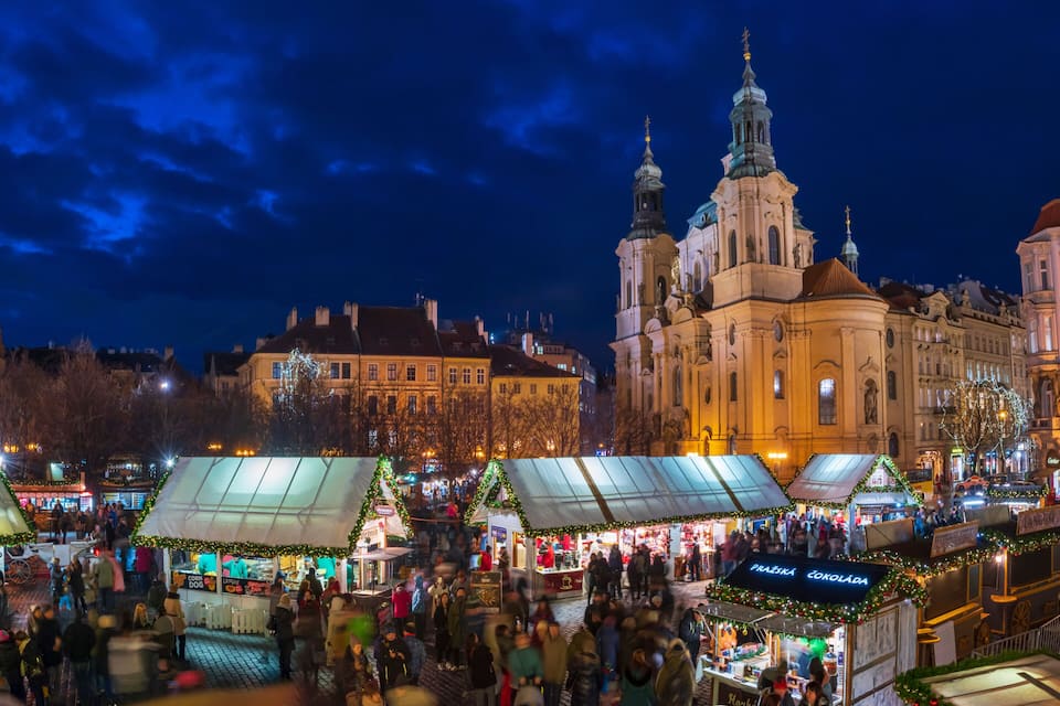 A bustling nighttime market with stalls and a prominent church in the background.
