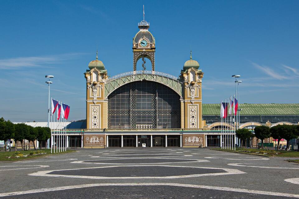 Ein prächtiges Gebäude mit einem Uhrturm, einem grossen Rundbogenportal und mehreren Flaggen.